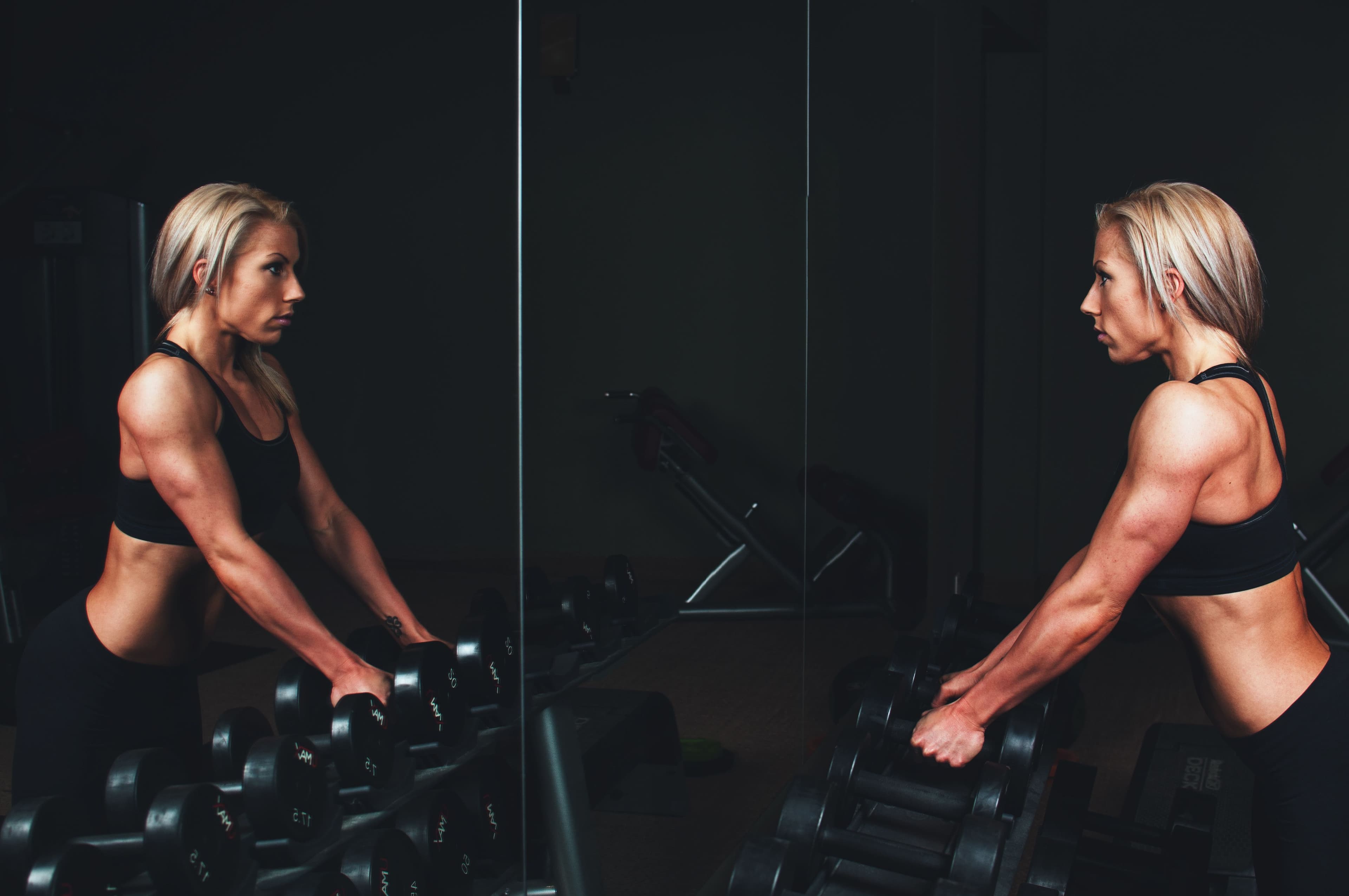 A woman lifting dumbbells, reflected in a gym mirror